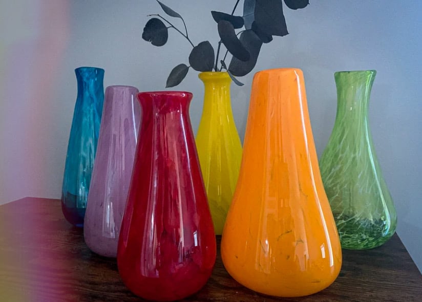 A collection of blue, lavender, red, yellow, orange, and green glass vases