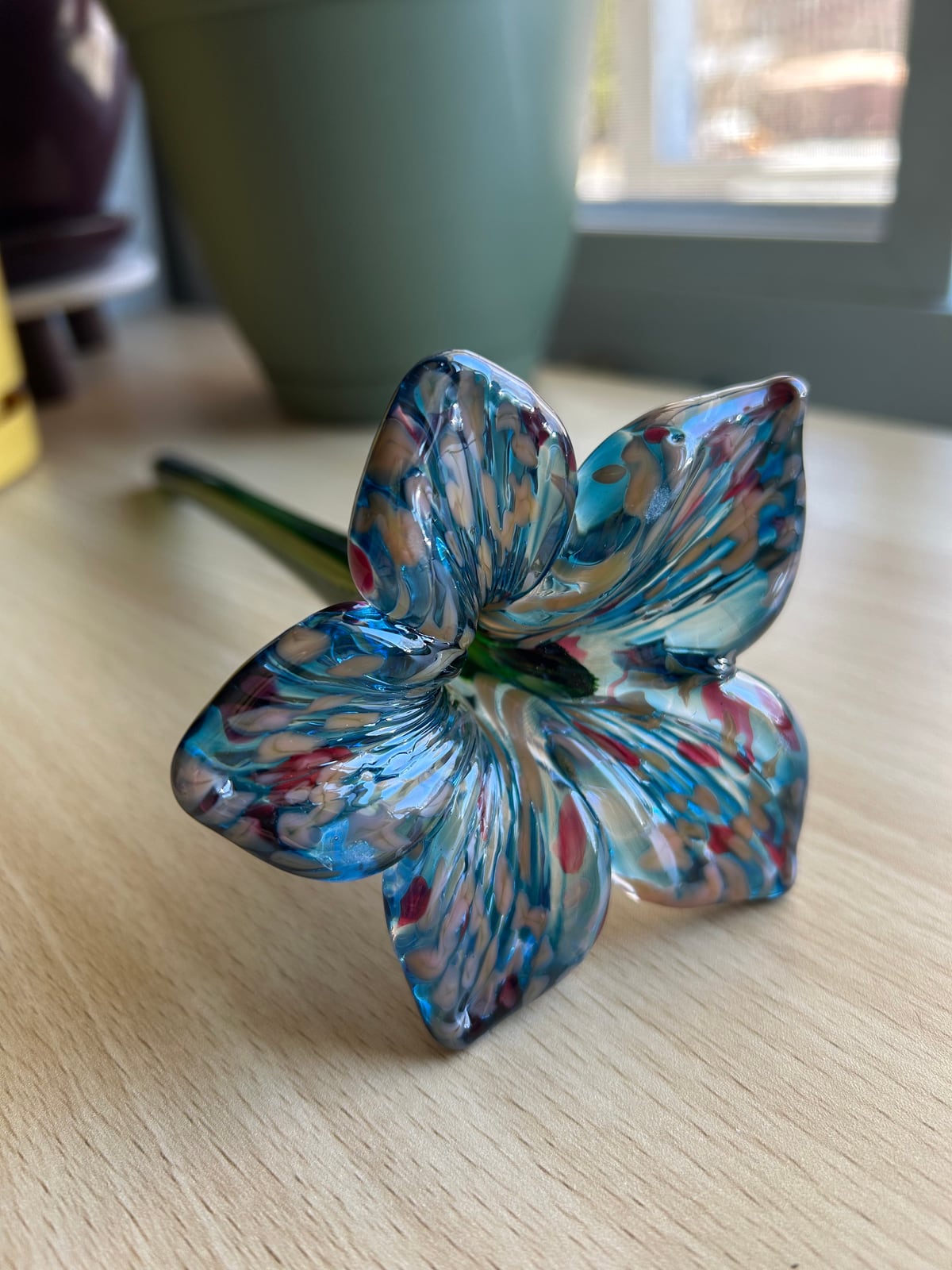 A glass flower with blue, white, and pink petals and a green stem