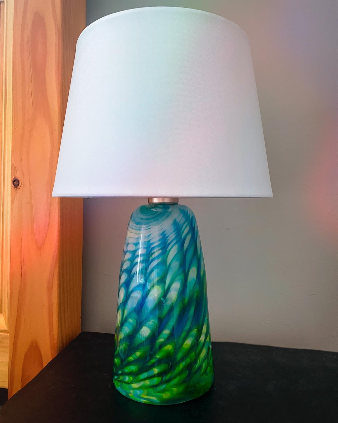 A glass lamp with a blue and green patterned base and a white shade